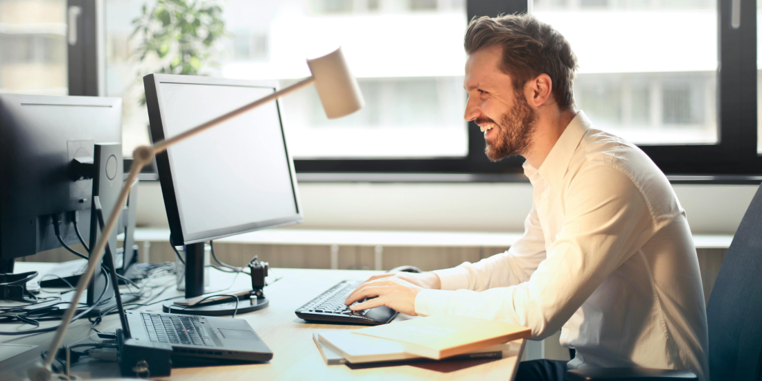 Estate agent sat at desk smiling at his computer screen