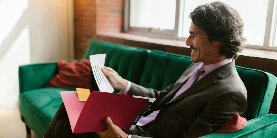 Male estate agent in suit smiling looking at holder while sat on sofa