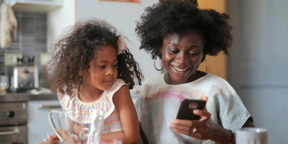 Woman looking at a self service portal on her phone while with her daughter
