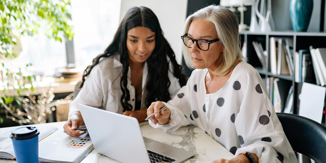 Older female estate agent helping a younger female estate agent on the laptop